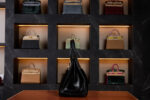 A luxurious black Hermès Birkin bag with palladium hardware and made with Horse Hair Troika displayed on a leather surface, set against a dark marble wall featuring a backlit collection of various Hermès handbags in different colors and materials.